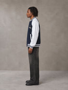 Model wearing the SM Varsity Jacket in Oxford Navy, side profile.