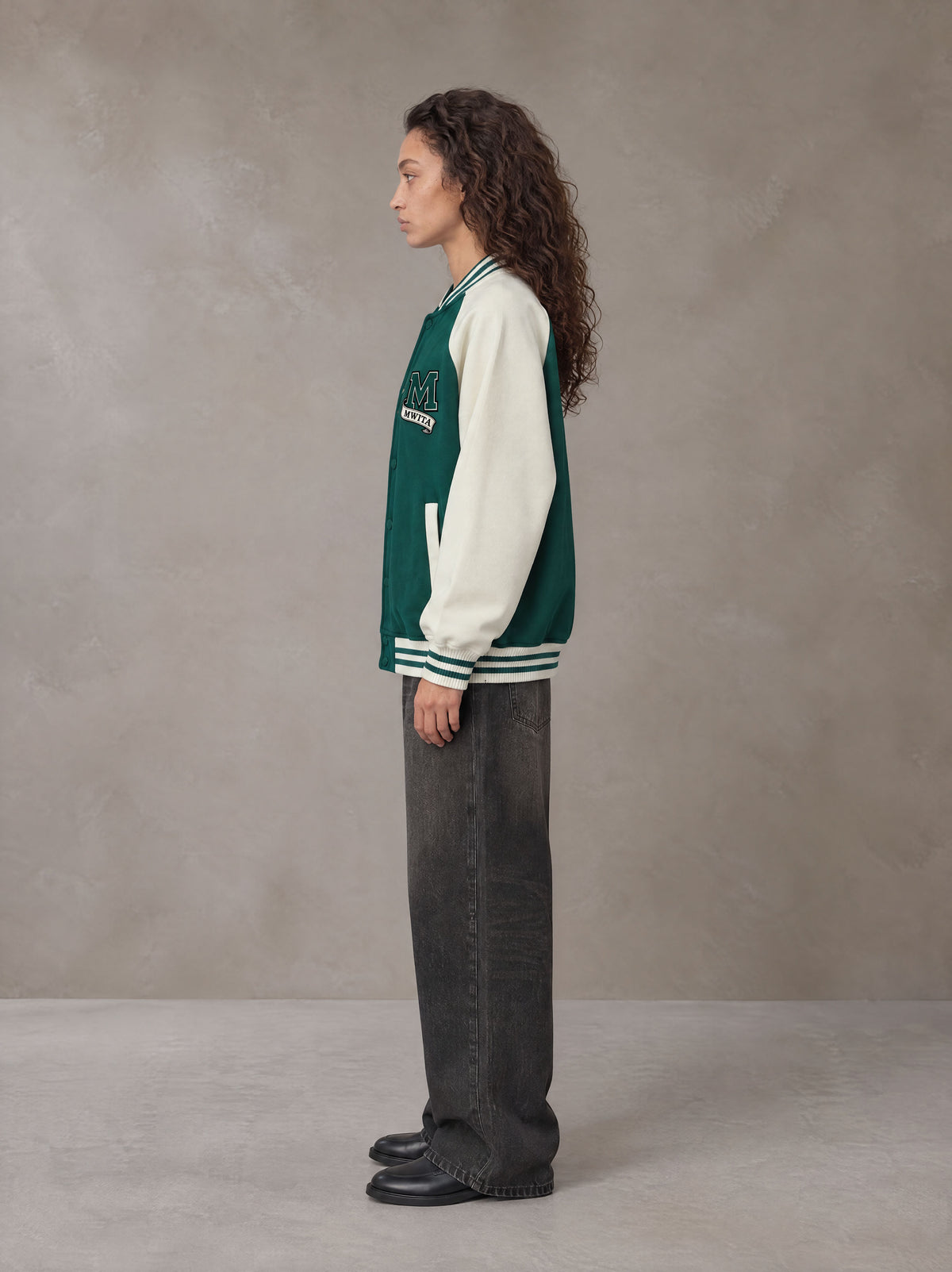 Model wearing the SM Varsity Jacket in Alpine Green, side profile.