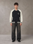 Model wearing the SM Varsity Jacket in Midnight Black, front view.