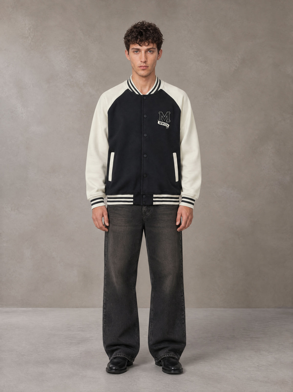 Model wearing the SM Varsity Jacket in Midnight Black, front view.