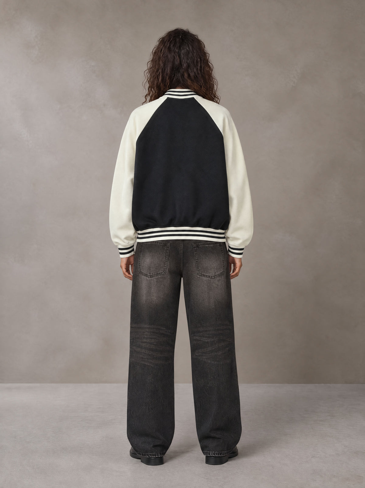 Model wearing the SM Varsity Jacket in Midnight Black, rear view.