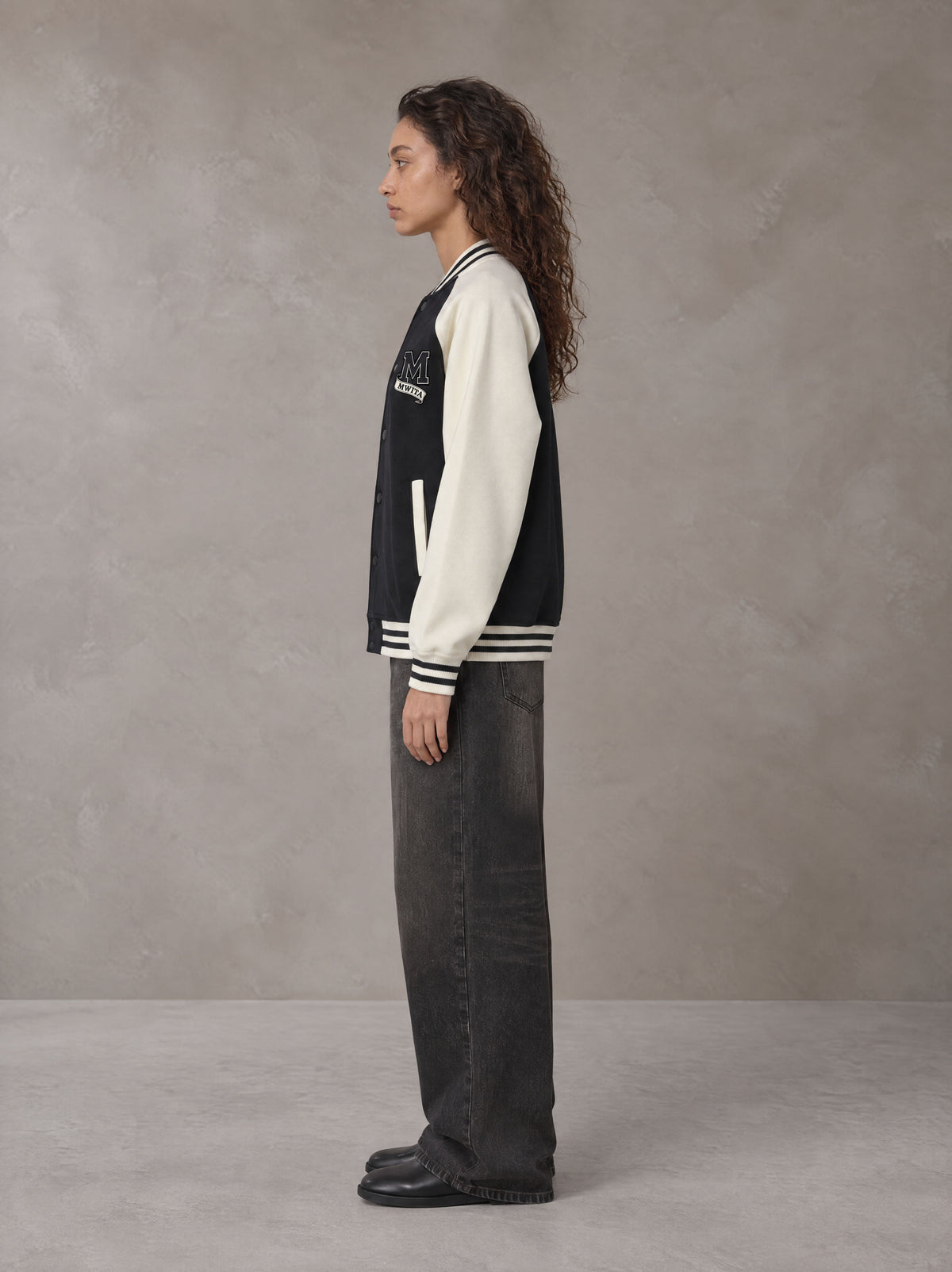 Model wearing the SM Varsity Jacket in Midnight Black, side profile.