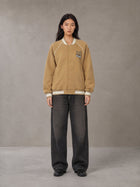 Model wearing the SM Varsity Jacket in Camel Tan, front view.