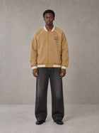 Model wearing the SM Varsity Jacket in Camel Tan, front view.