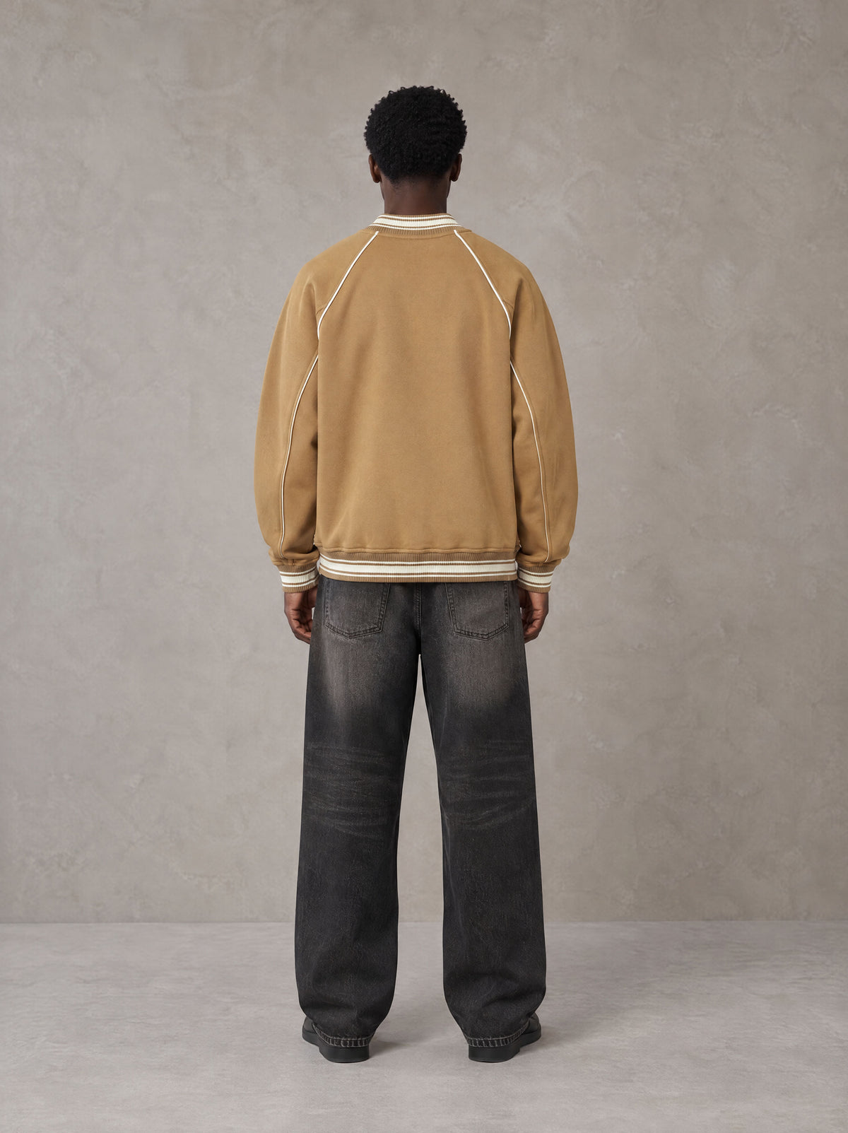 Model wearing the SM Varsity Jacket in Camel Tan, rear view.