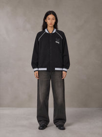 Model wearing the SM Varsity Jacket in Midnight Black, front view.