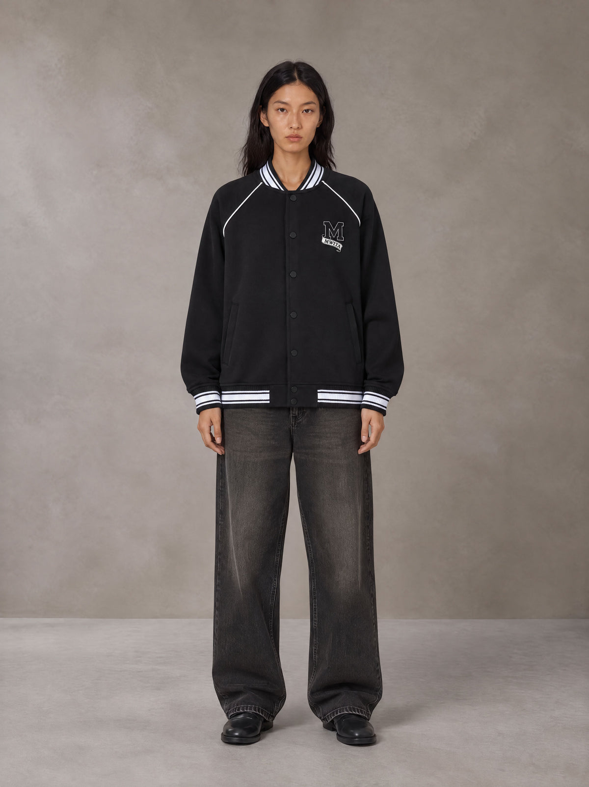 Model wearing the SM Varsity Jacket in Midnight Black, front view.