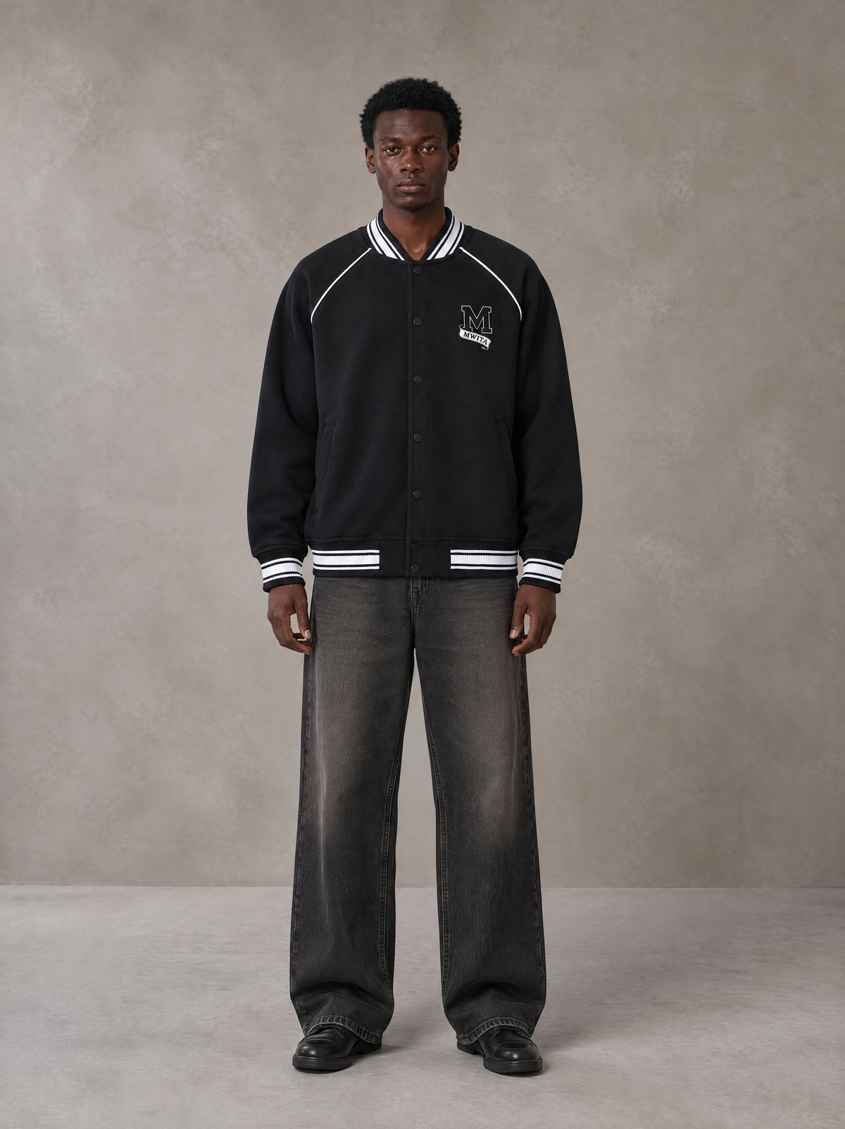Model wearing the SM Varsity Jacket in Midnight Black, front view.