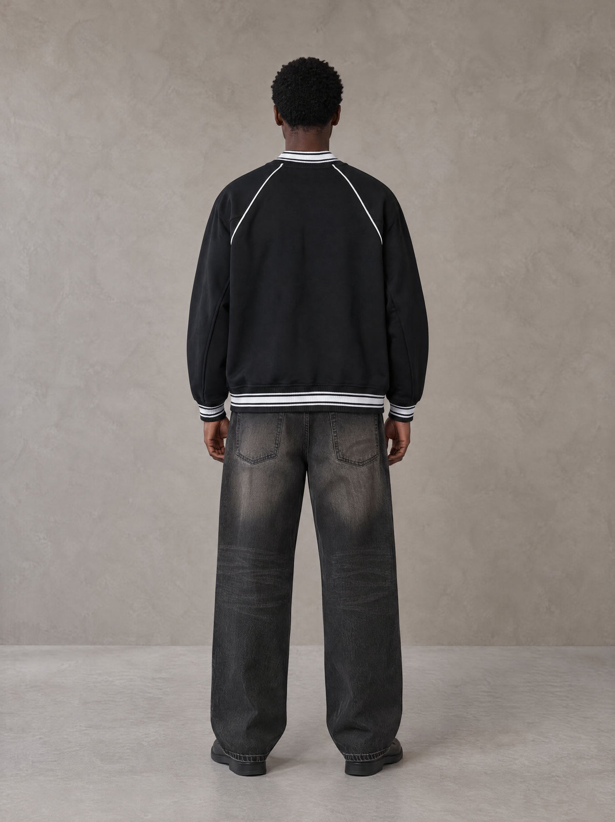 Model wearing the SM Varsity Jacket in Midnight Black, rear view.