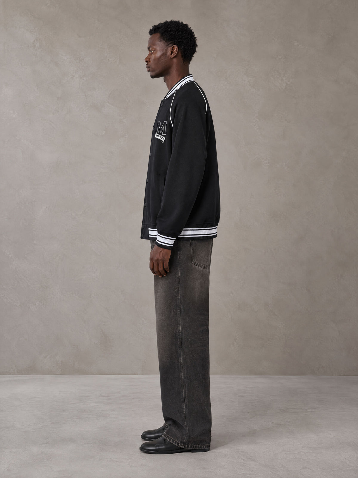 Model wearing the SM Varsity Jacket in Midnight Black, side profile.