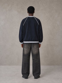 Model wearing the SM Varsity Jacket in Oxford Navy, rear view.