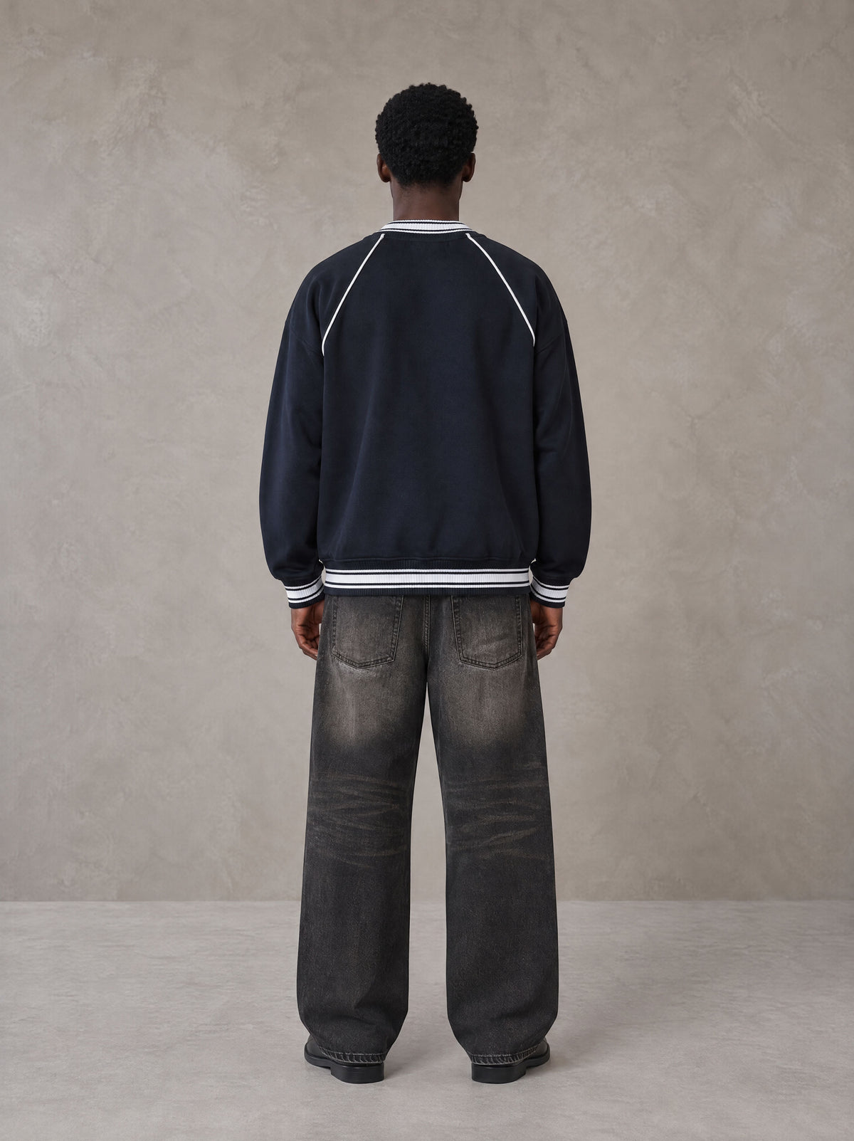 Model wearing the SM Varsity Jacket in Oxford Navy, rear view.