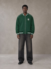 Model wearing the SM Varsity Zip Jacket in Alpine Green, front view.
