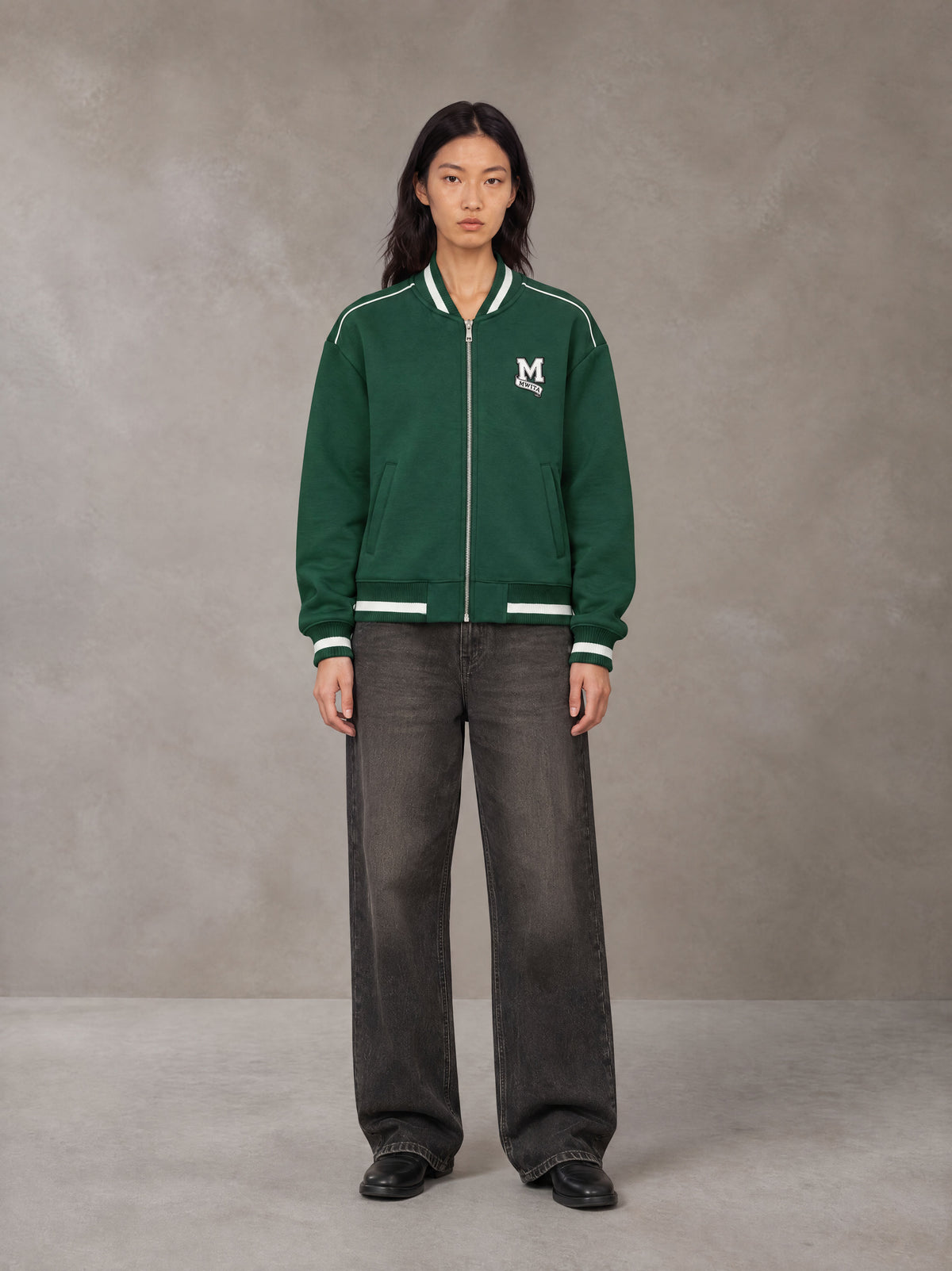 Model wearing the SM Varsity Zip Jacket in Alpine Green, front view.