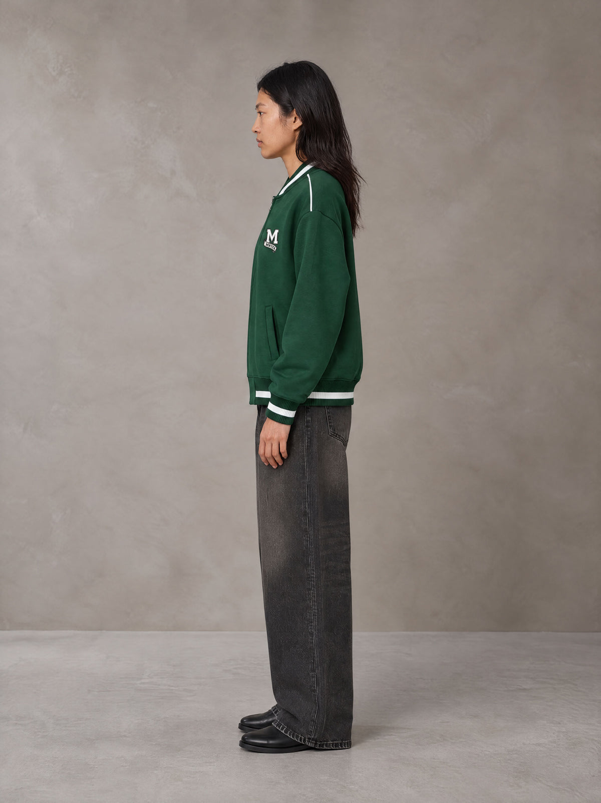 Model wearing the SM Varsity Zip Jacket in Alpine Green, side profile.
