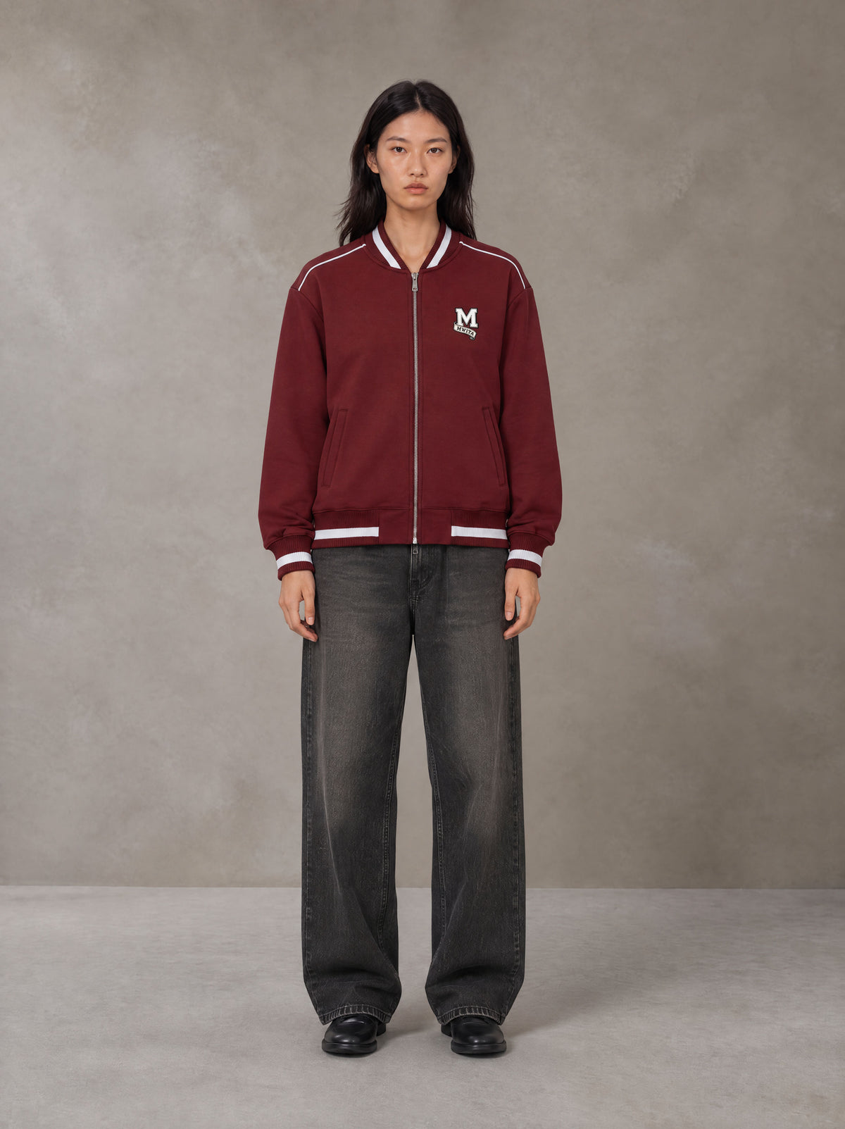 Model wearing the SM Varsity Zip Jacket in Burgundy, front view.