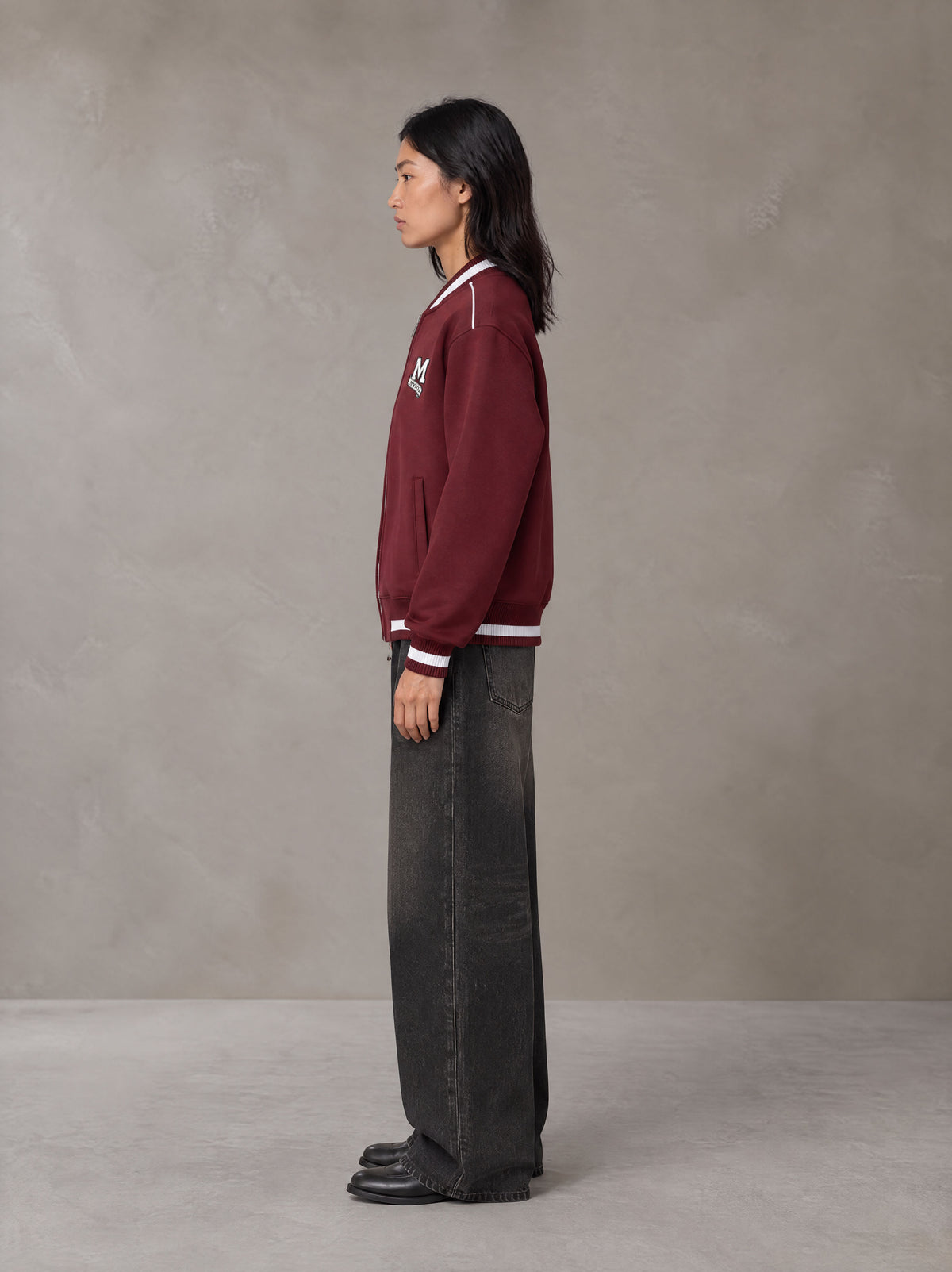 Model wearing the SM Varsity Zip Jacket in Burgundy, side profile.