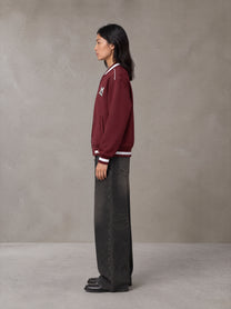 Model wearing the SM Varsity Zip Jacket in Burgundy, side profile.