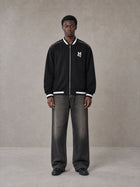 Model wearing the SM Varsity Zip Jacket in Midnight Black, front view.