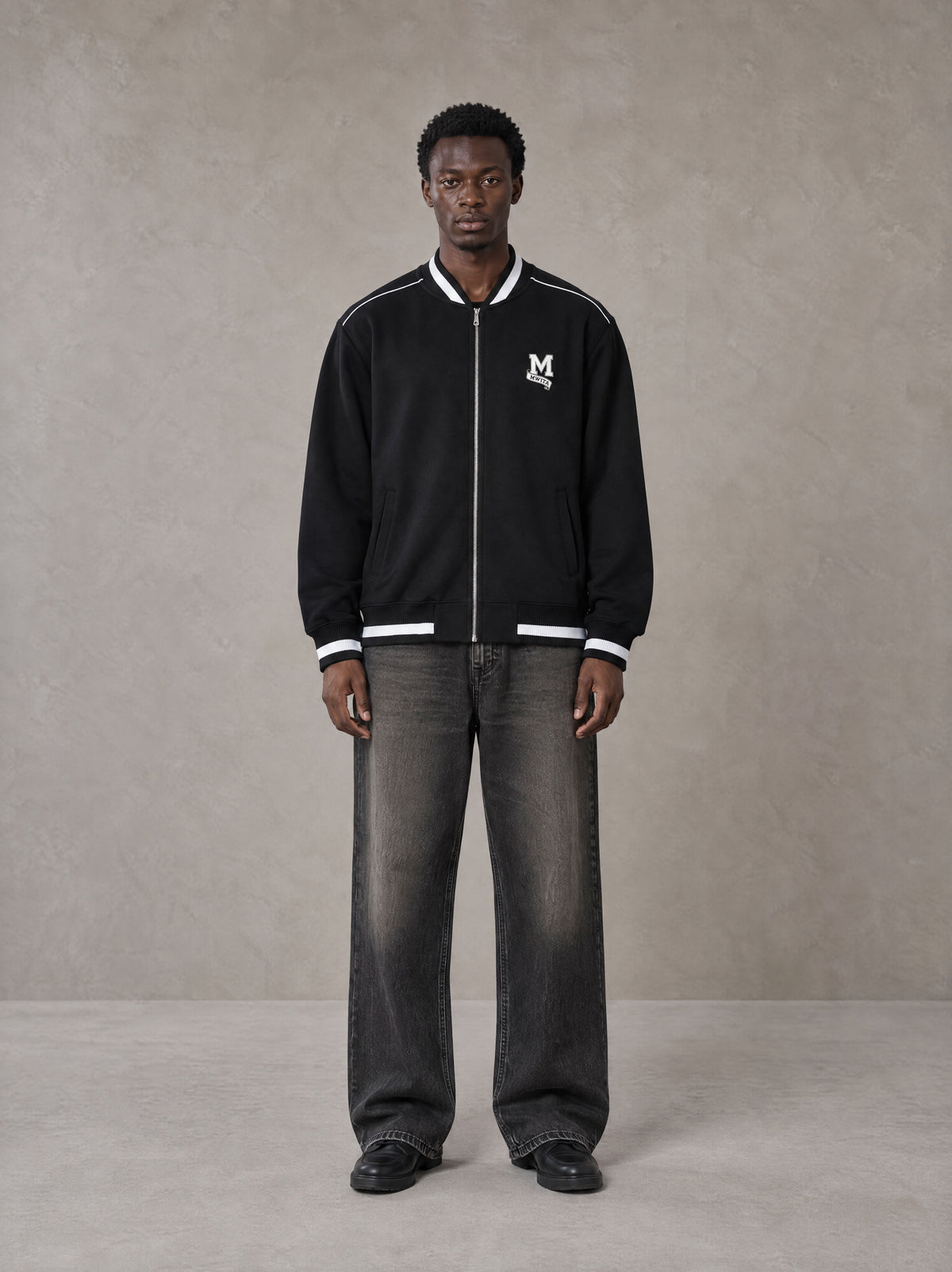 Model wearing the SM Varsity Zip Jacket in Midnight Black, front view.
