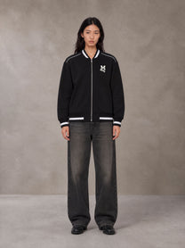 Model wearing the SM Varsity Zip Jacket in Midnight Black, front view.