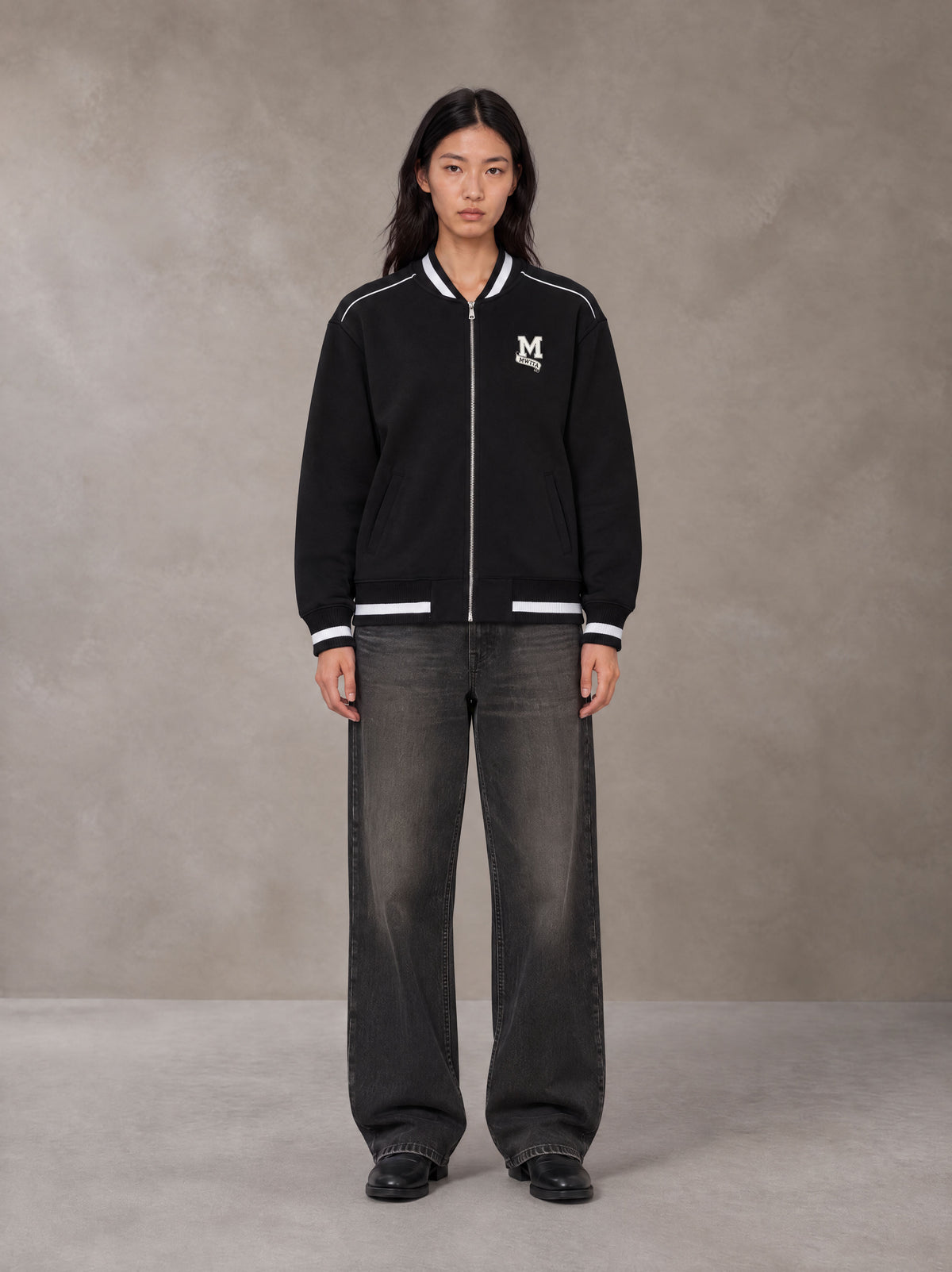 Model wearing the SM Varsity Zip Jacket in Midnight Black, front view.