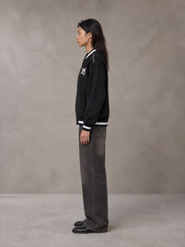 Model wearing the SM Varsity Zip Jacket in Midnight Black, side profile.