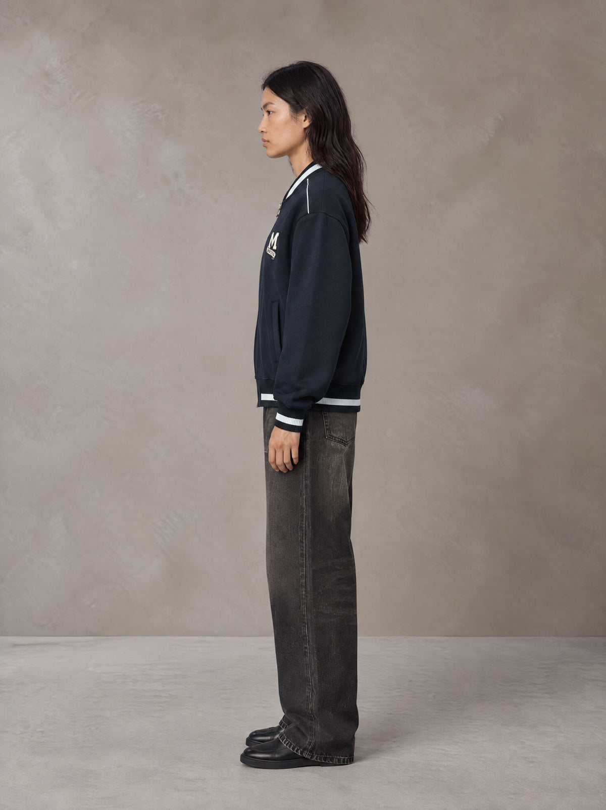 Model wearing the SM Varsity Zip Jacket in Oxford Navy, side profile.