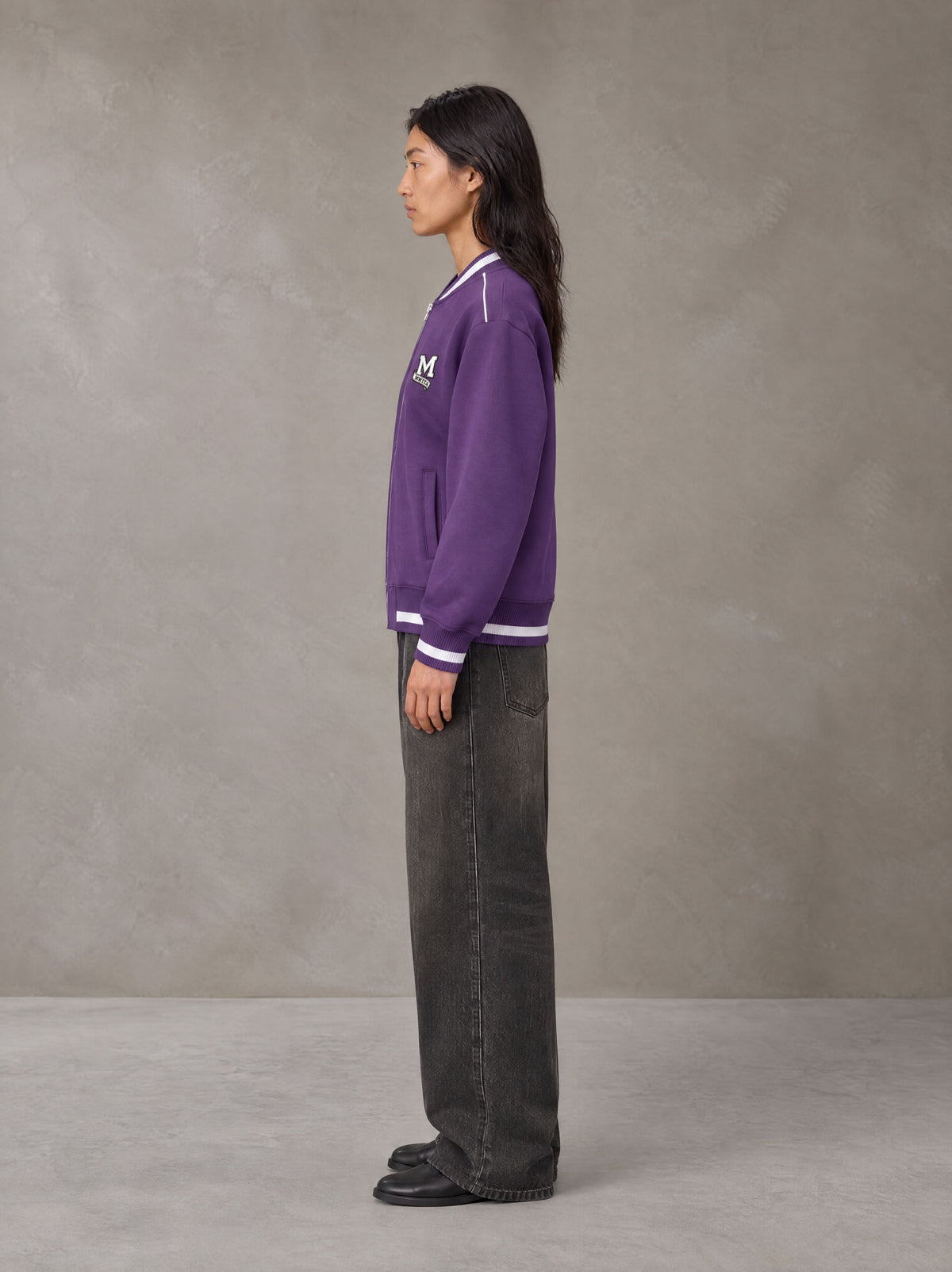 Model wearing the SM Varsity Zip Jacket in Rich Violet, side profile.