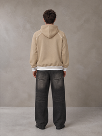 Model wearing the SM Insignia Hoodie in Oatmeal Cookie, rear view.