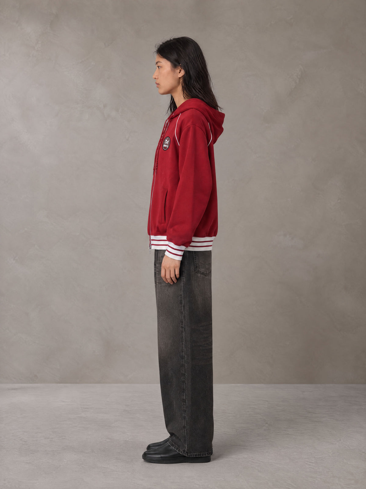 Model wearing the SM Insignia Hoodie in Carmine, side profile.