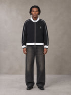 Model wearing the SM Insignia Trim Track Jacket in Midnight Black, front view.