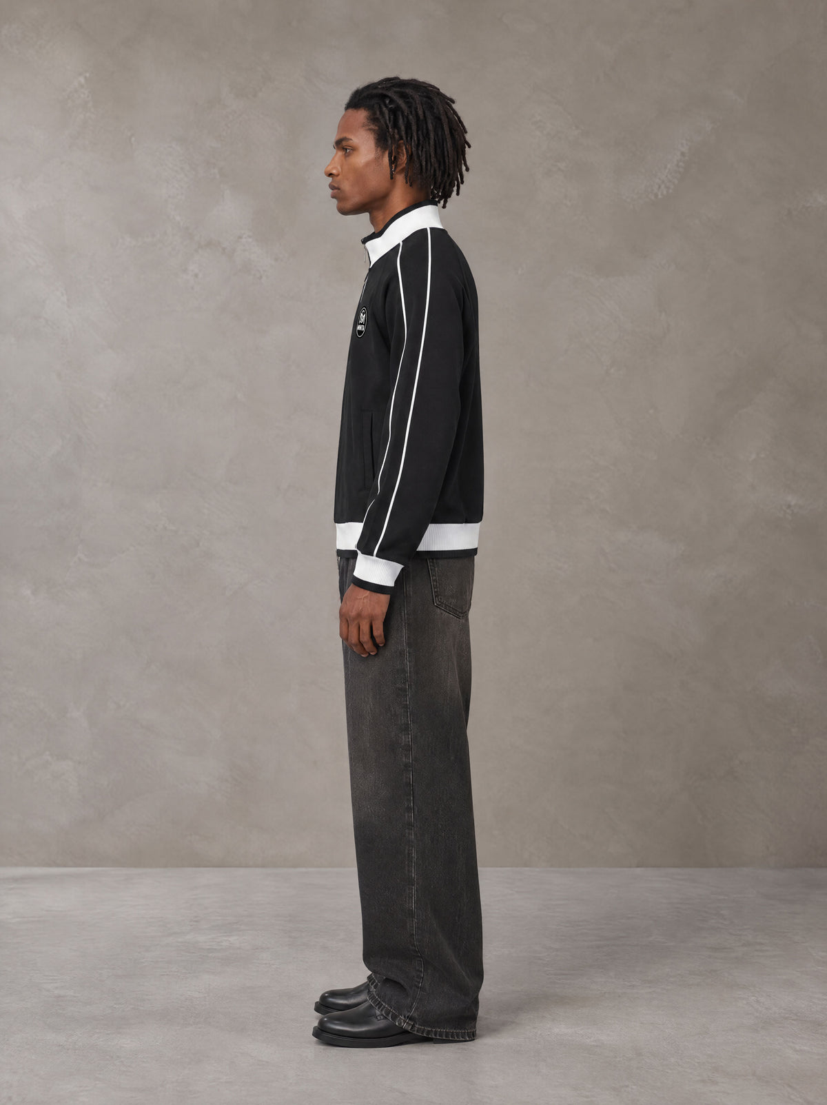 Model wearing the SM Insignia Trim Track Jacket in Midnight Black, side profile.