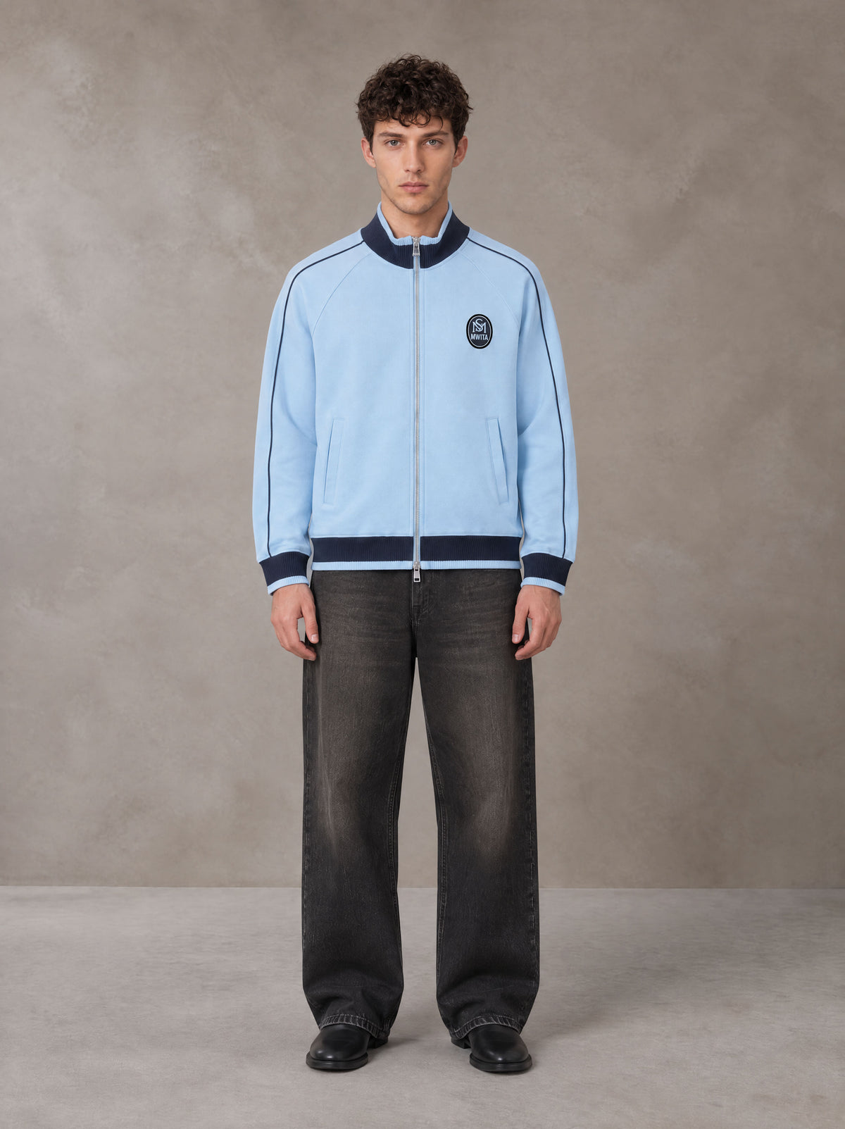 Model wearing the SM Insignia Trim Track Jacket in Sky Tint, front view.