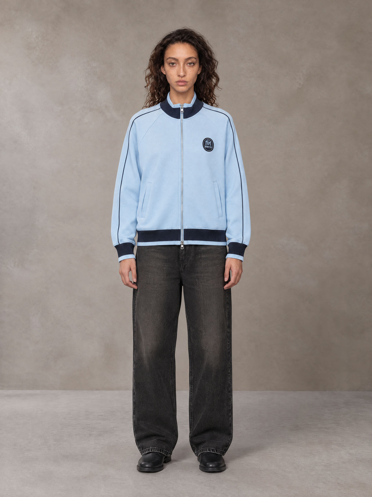 Model wearing the SM Insignia Trim Track Jacket in Sky Tint, front view.