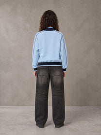 Model wearing the SM Insignia Trim Track Jacket in Sky Tint, rear view.