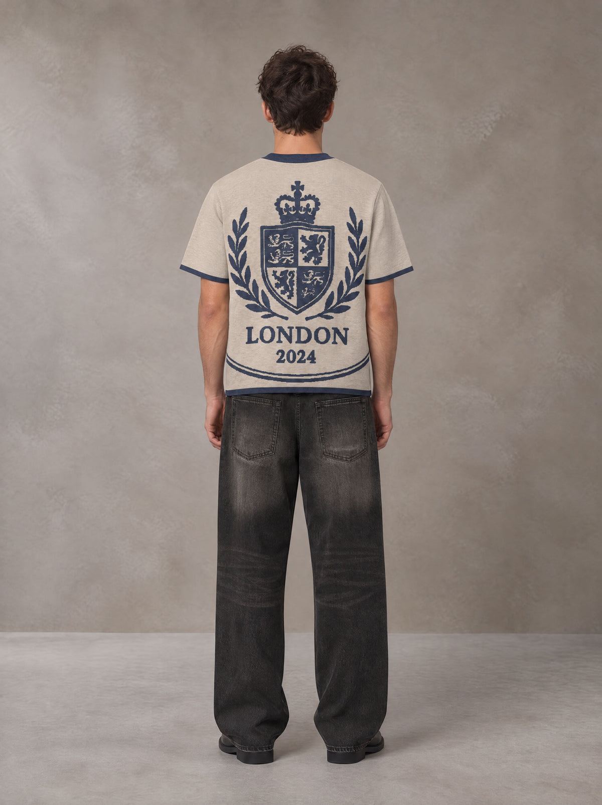 Model wearing the SM Jacquard Knitted Royal Emblem Knitted T-shirt in Oatmeal Cookie, rear view.