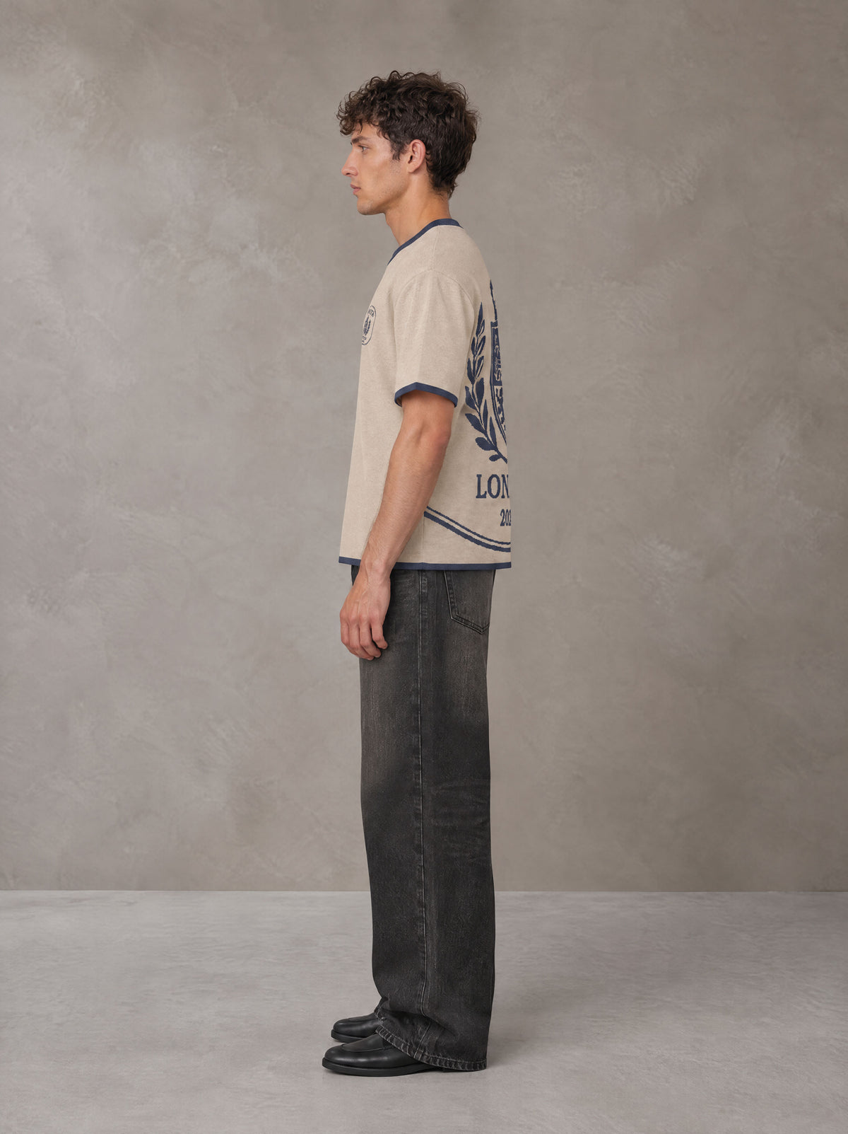 Model wearing the SM Jacquard Knitted Royal Emblem Knitted T-shirt in Oatmeal Cookie, side profile.