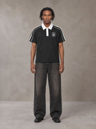 Model wearing the SM Royal Emblem Polo T-shirt in Midnight Black, front view.