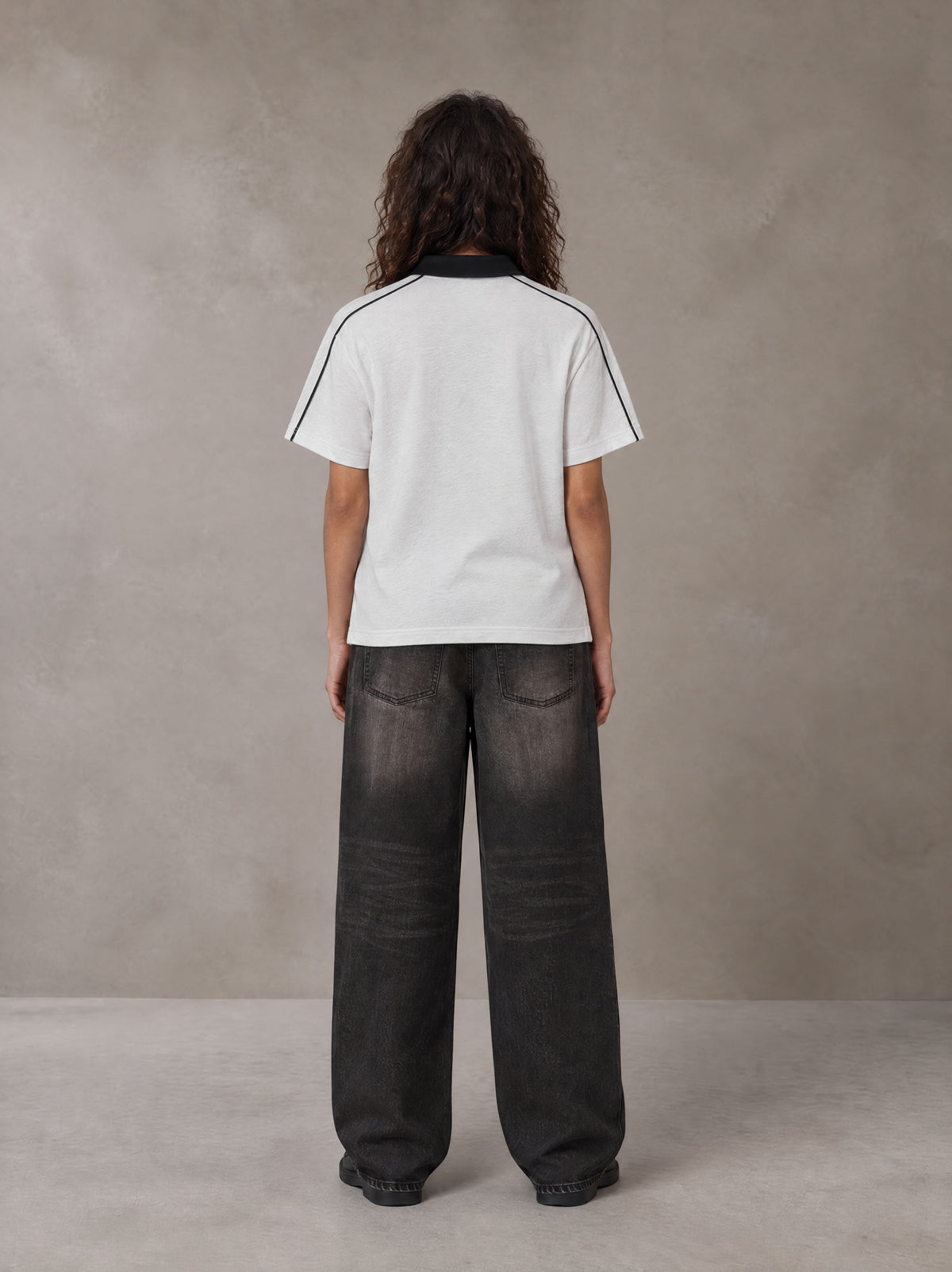 Model wearing the SM Royal Emblem Polo T-shirt in Floral Grey, rear view.