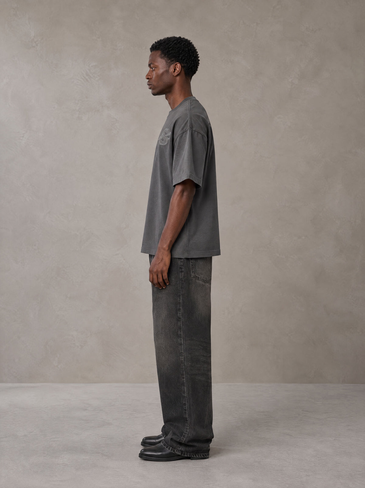 Model wearing the SM Carved Flight T-shirt in Deep Charcoal, side profile.