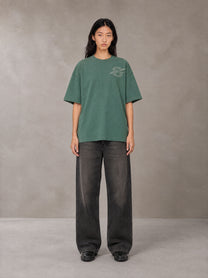 Model wearing the SM Carved Flight T-shirt in Forest Deep, front view.