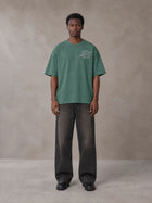 Model wearing the SM Carved Flight T-shirt in Forest Deep, front view.
