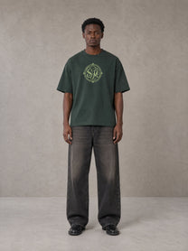 Model wearing the SM Emblem T-shirt in Dark Green, front view.
