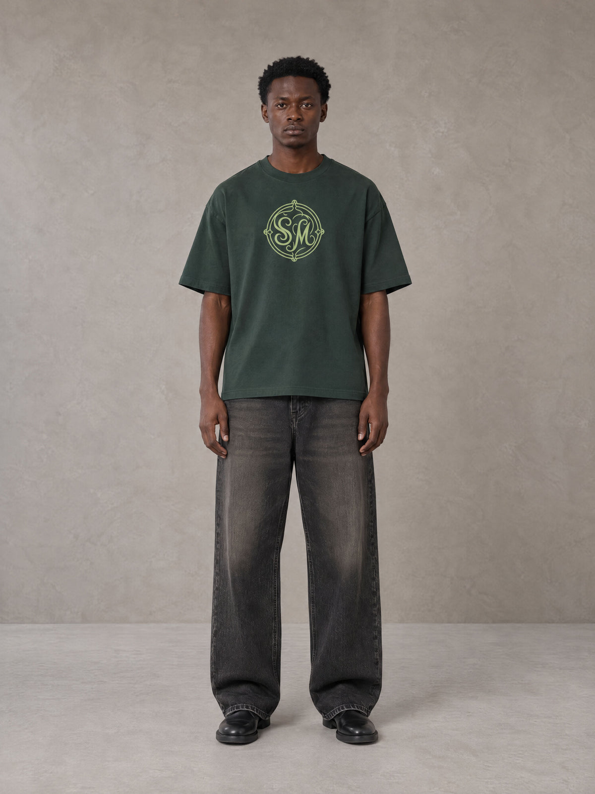 Model wearing the SM Emblem T-shirt in Dark Green, front view.