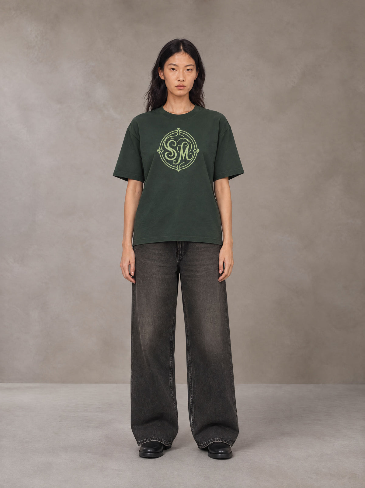 Model wearing the SM Emblem T-shirt in Dark Green, front view.