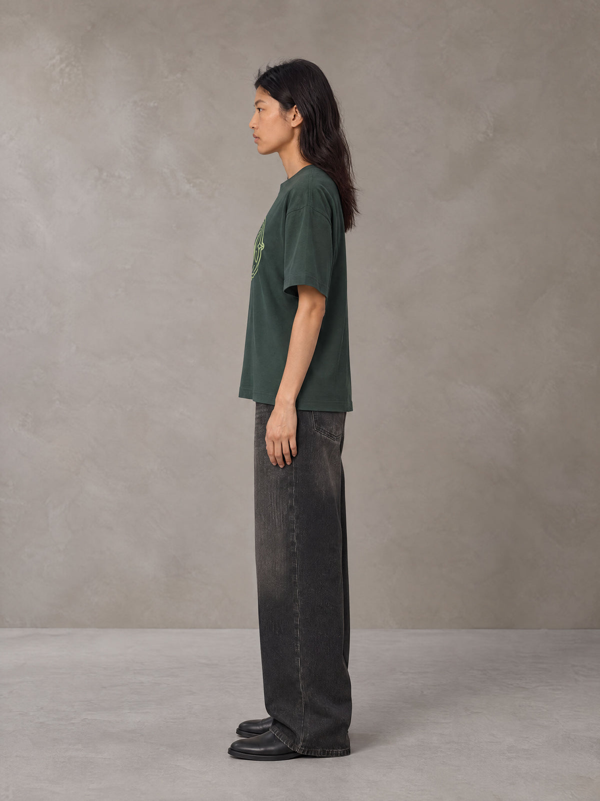 Model wearing the SM Emblem T-shirt in Dark Green, side profile.
