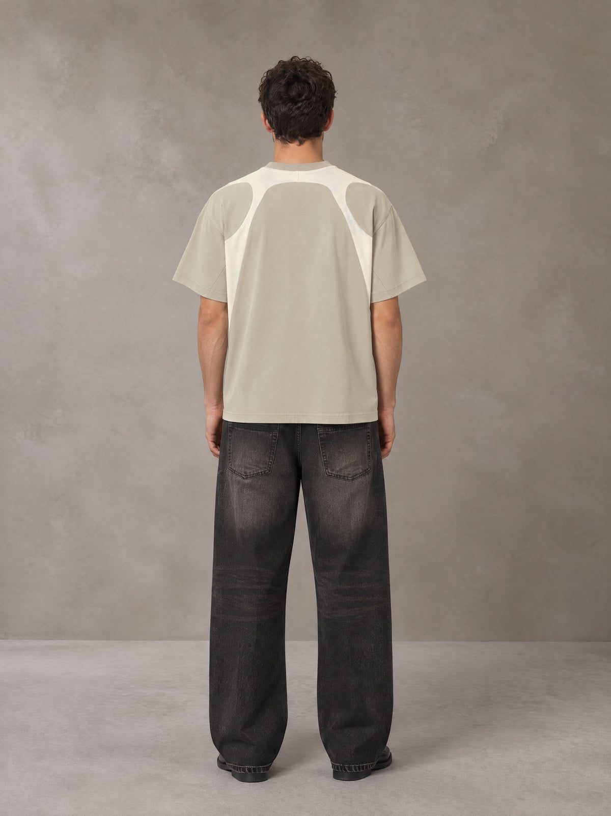 Model wearing the SM Graffiti Stack T-shirt in Oatmeal Cookie, rear view.