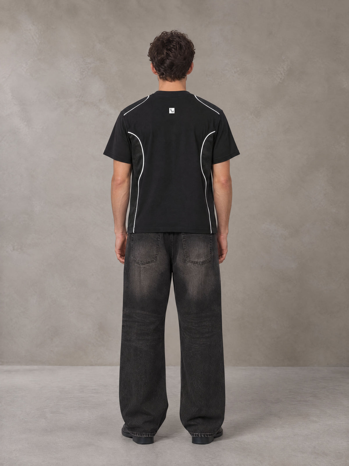 Model wearing the SM Legacy Jersey T-shirt in Midnight Black, rear view.
