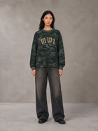 Model wearing the SM Script Camo Long Sleeve T-shirt in Jungle Green, front view.
